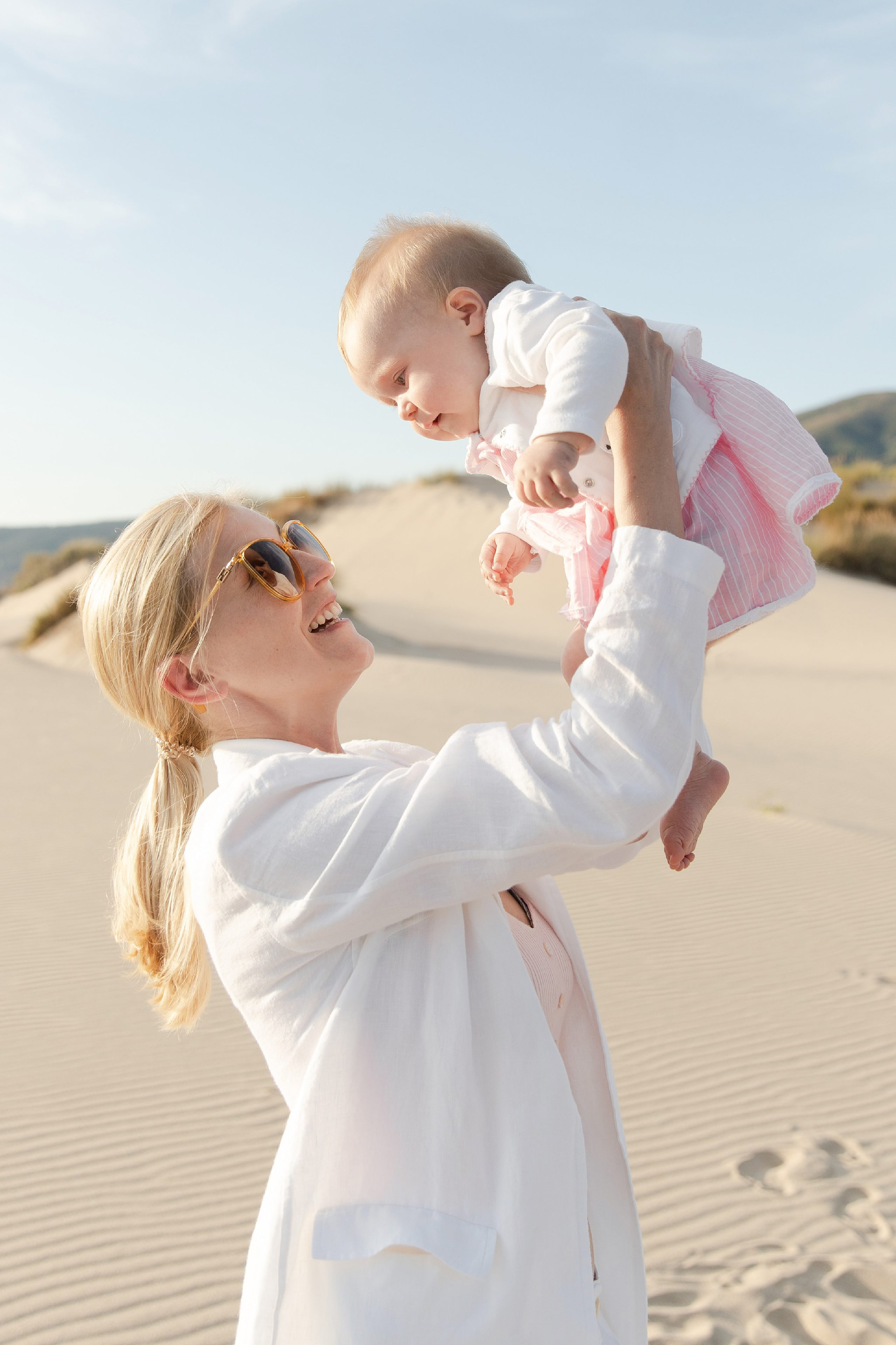 Mother lifting her baby daughter in the dunes at Guincho, Portugal