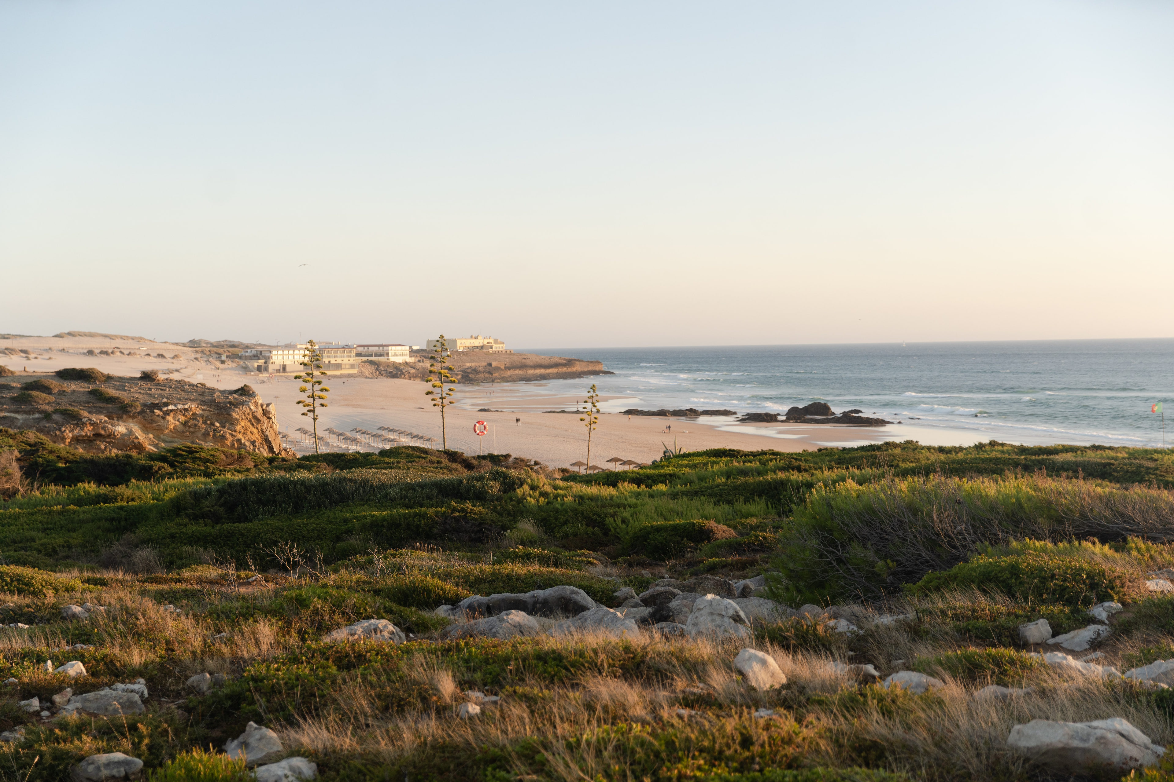 Guincho beach in evening light beyond green coastal scrub, the Atlantic to the right, Cascais Guincho beach in evening light beyond green coastal scrub, the Atlantic to the right, Cascais