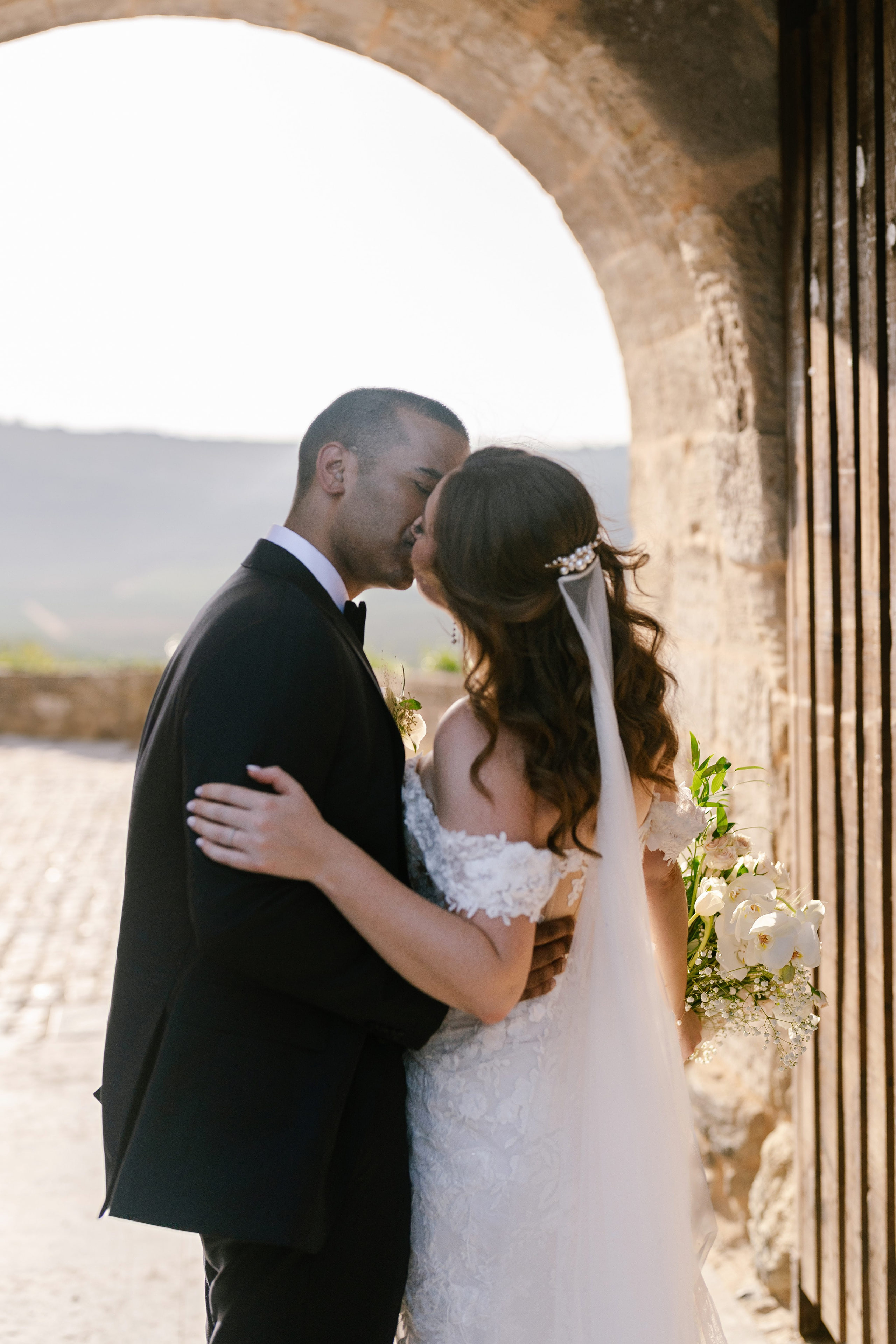 Bride and groom kissing under a stone arch in Óbidos, Portugal