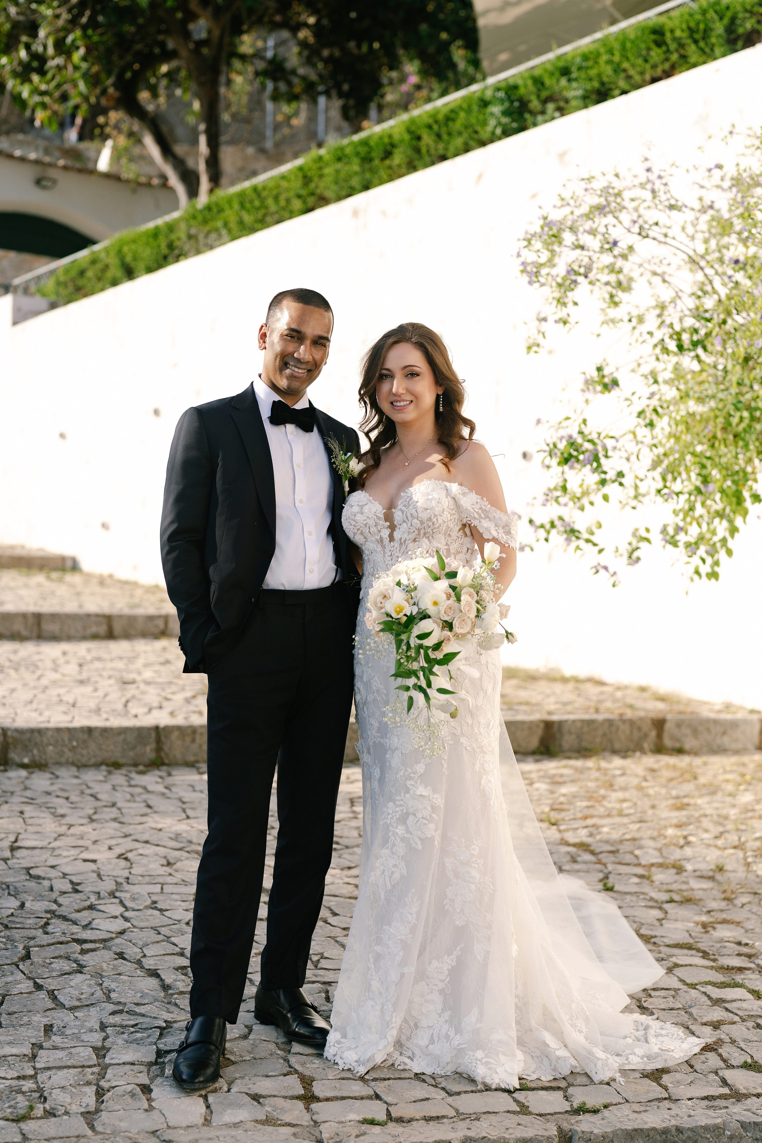 Bride and groom standing together on cobblestone steps with whitewashed walls and greenery in Óbidos, Portugal Bride and groom standing together on cobblestone steps with whitewashed walls and greenery in Óbidos, Portugal