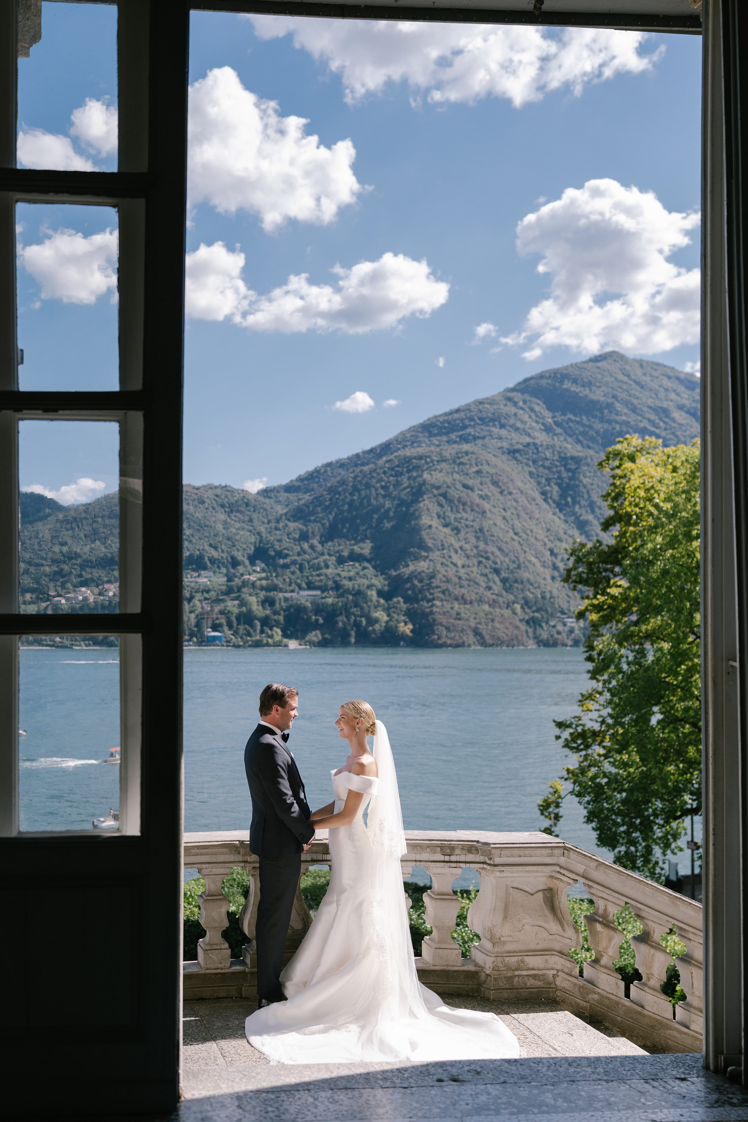 Bride and groom framed by an open window of Villa Carlotta, with Lake Como behind