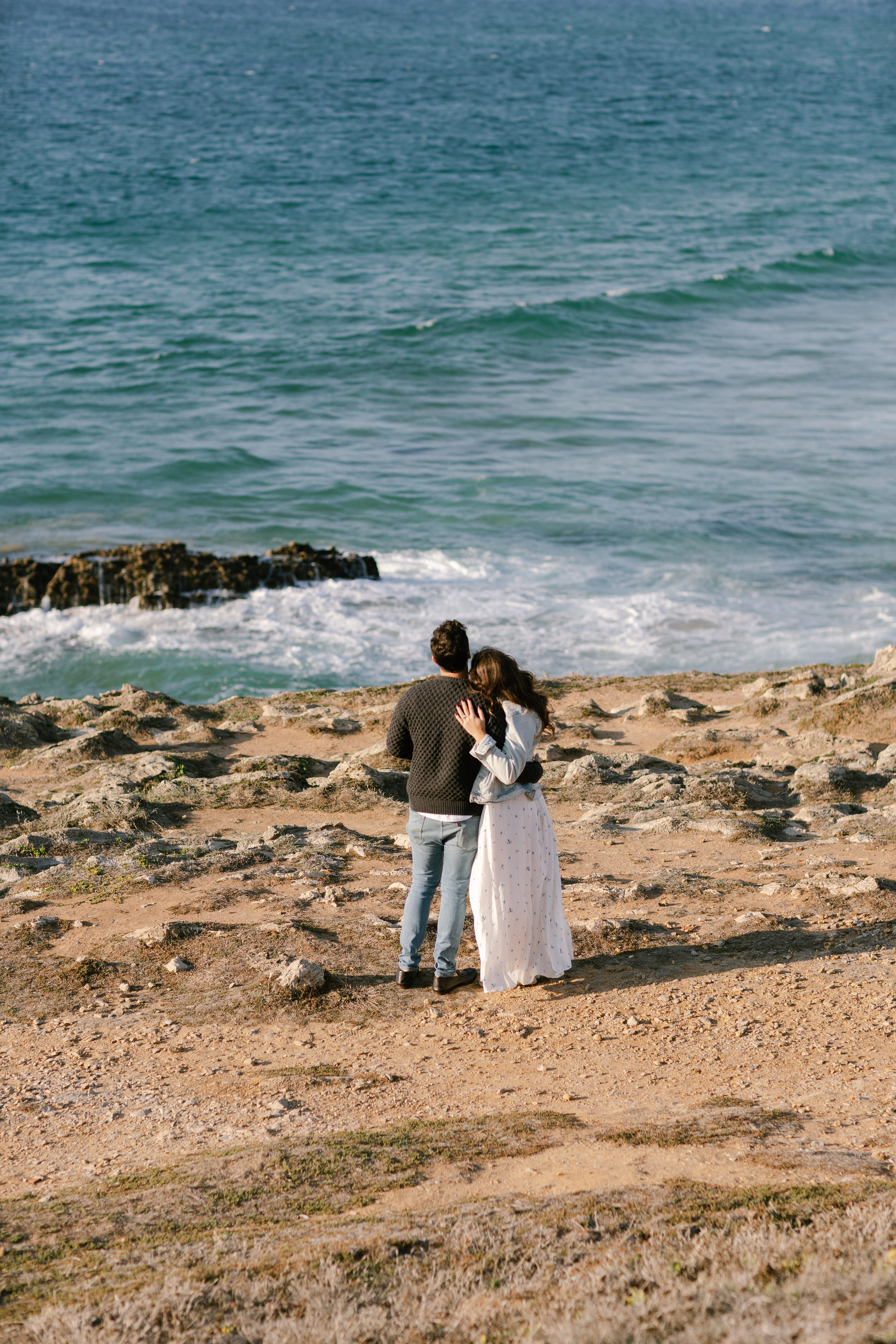Couple on the rocks above the sea at Guincho, Cascais, he in a dark sweater, she in a long white dress Couple on the rocks above the sea at Guincho, Cascais, he in a dark sweater, she in a long white dress