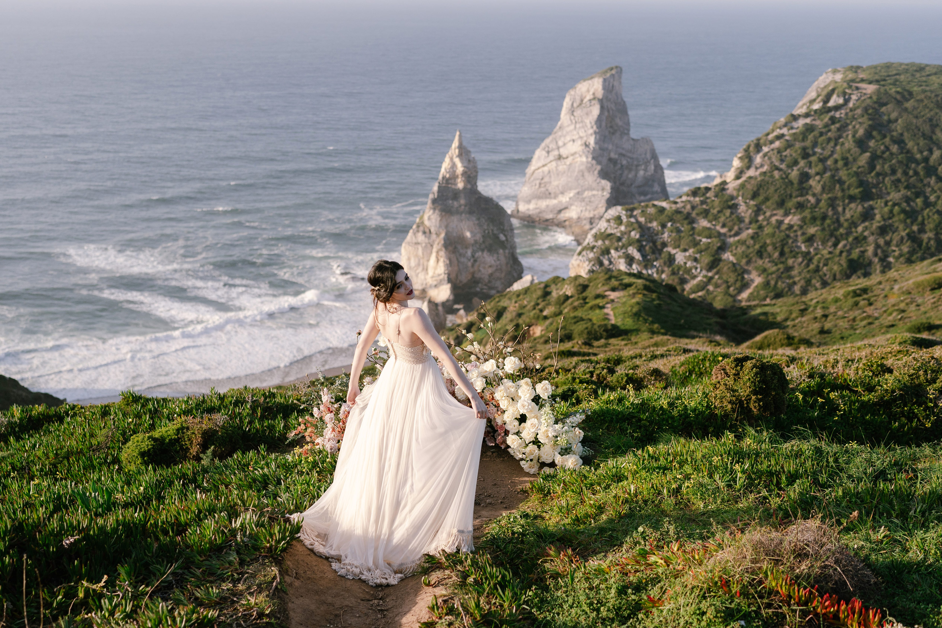 Bride walking along the clifftop above Praia da Ursa, with the sea stacks behind her
