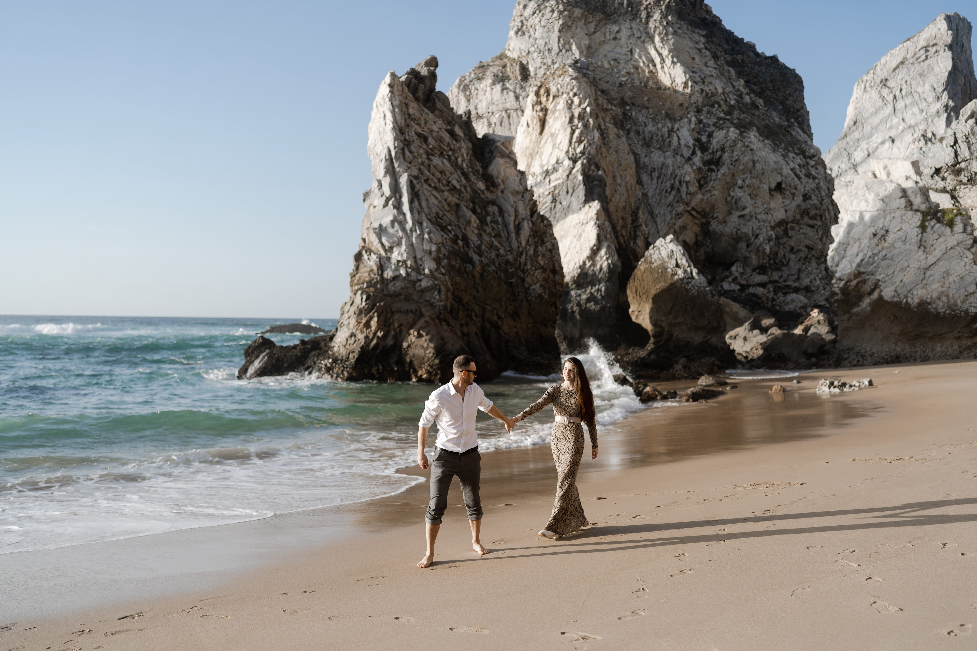 Couple walking hand in hand between the sea stacks of Praia da Ursa, Sintra