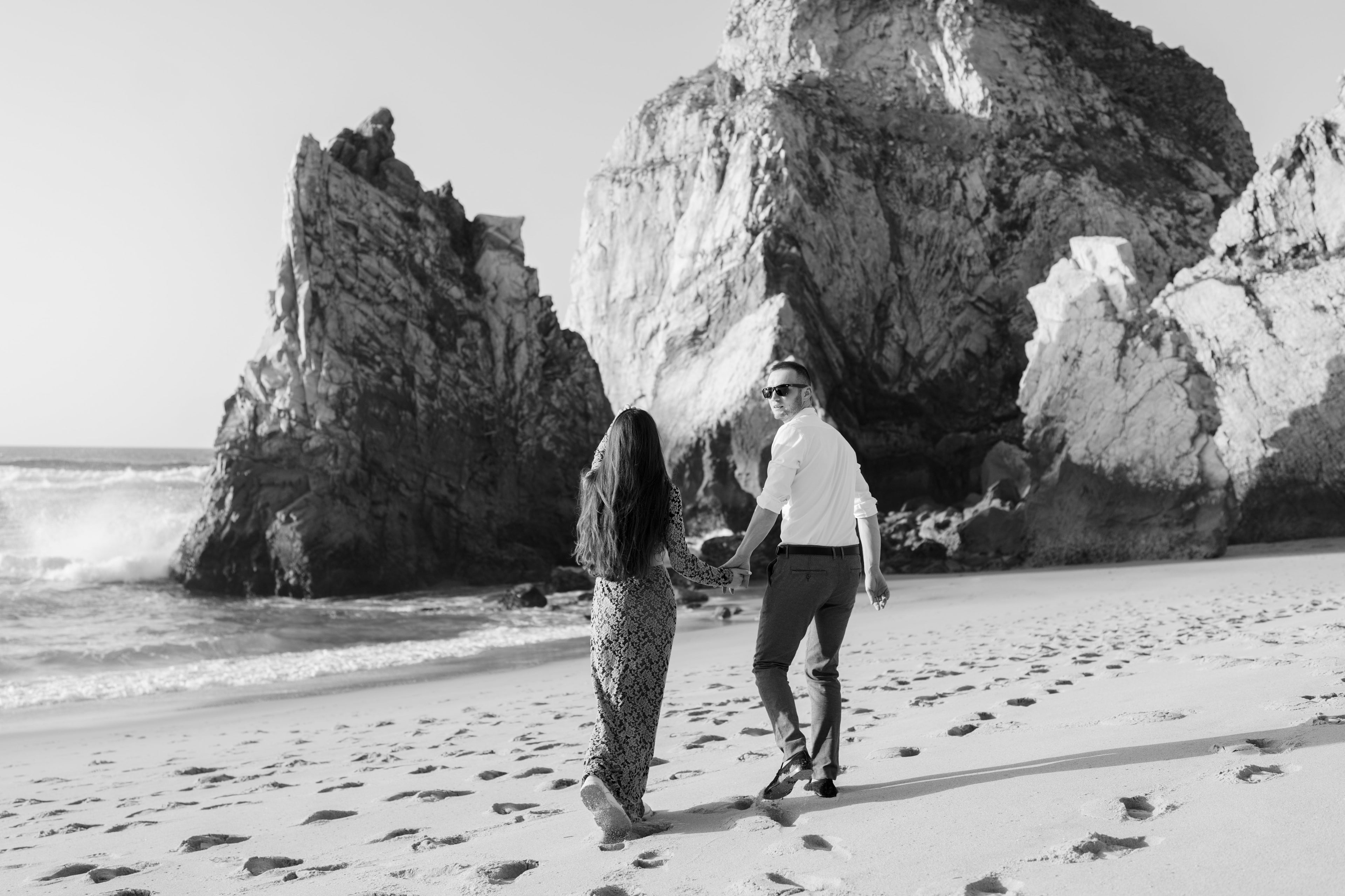 Couple walking between the rocks of Praia da Ursa, in black and white