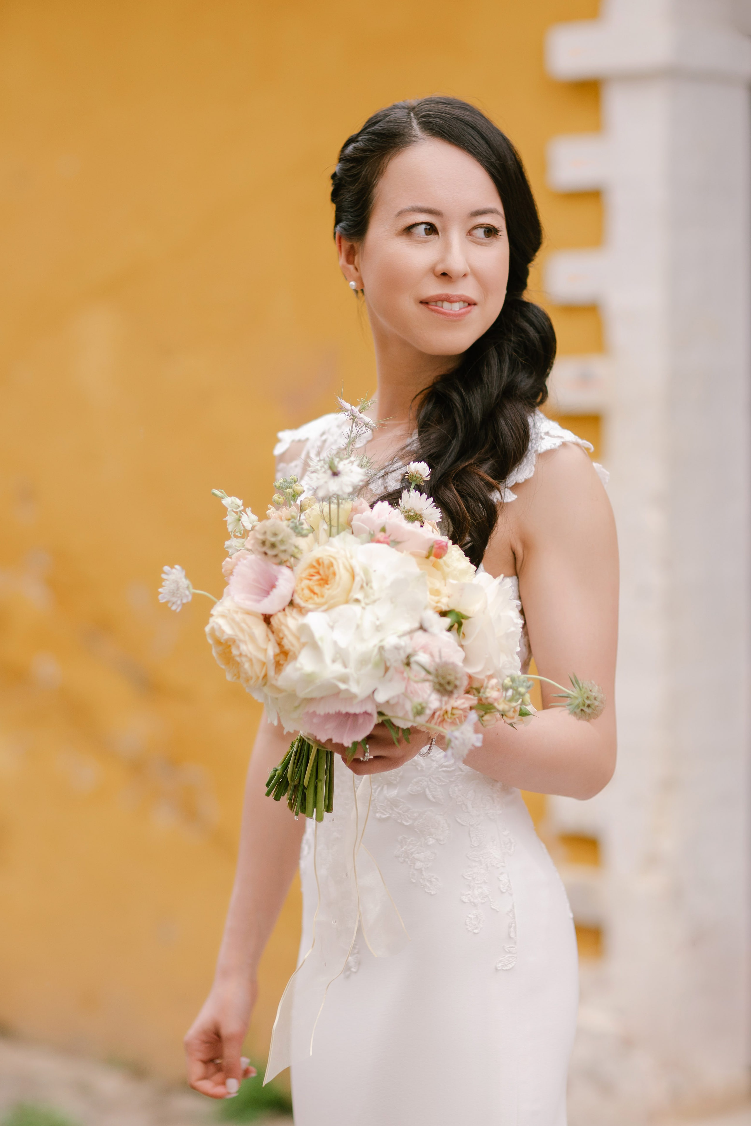 Bride posing with her pastel wedding bouquet in front of a textured yellow wall at Quinta de Sant’Ana Bride posing with her pastel wedding bouquet in front of a textured yellow wall at Quinta de Sant’Ana